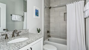Un baño con lavamanos de encimera de granito, inodoro blanco y bañera.