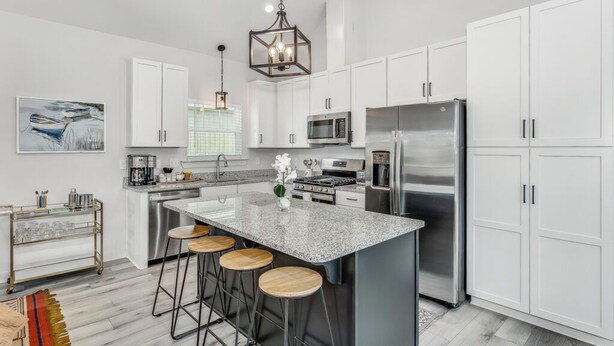 Una cocina moderna con gabinetes blancos, electrodomésticos de acero inoxidable y una isla central con taburetes.