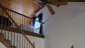Una escalera de madera con un ventilador de techo, una mesa con sillas y una pequeña ancla decorativa en la pared.
