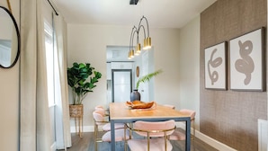A dining area with a wooden table, pink upholstered chairs, a hanging light fixture, and wall art. - La Vie Boheme, Cozy, Minutues to Coconut Grove (Miami)