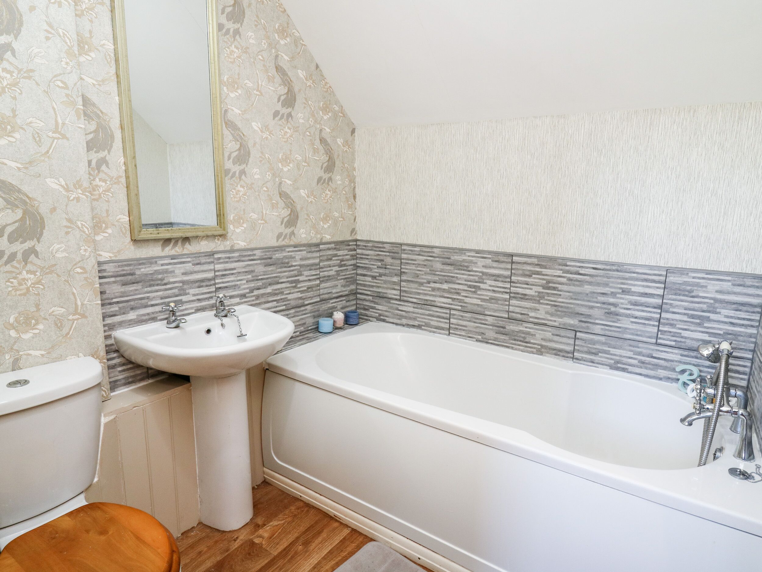 A bathroom with a white bathtub, a sink, and a toilet. The walls have a floral wallpaper and a tiled backsplash.