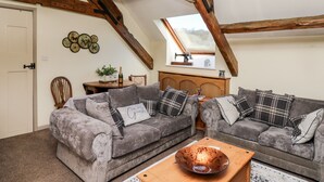 Ein Zimmer im Loft-Stil mit freiliegenden Holzbalken, einem Schlafplatz in der Erhöhung, einem Esstisch mit Stühlen und einem großen Fenster.