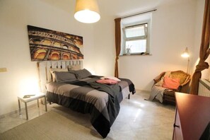 A bedroom with a bed, a small table, a chair, a window, and a painting on the wall. - Rome Trastevere Holidays Apartment (Roma)