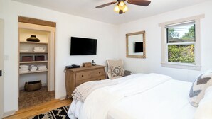 A bedroom with a bed, a ceiling fan, a television, a dresser, a mirror, and a window with a view of greenery. - Finca Mapache by Kokopelli Property Management (Santa Fe)