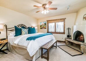 A bedroom with a bed, a ceiling fan, a window, a fireplace, and a nightstand.