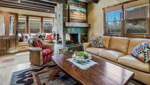 A cozy living room with a fireplace, leather sofa, and a wooden coffee table. - Finca Mapache by Kokopelli Property Management (Santa Fe)