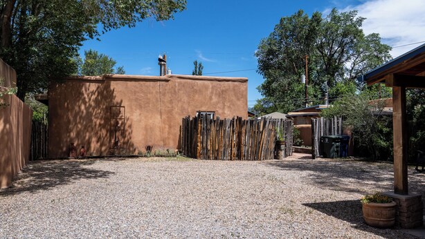 A courtyard with a gravel ground, a wooden fence, and a building with a chimney. - Finca Mapache by Kokopelli Property Management (Santa Fe)