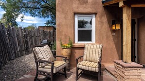 An outdoor patio area with two cushioned chairs and a small table, a wooden fence, and a stone pathway. - Finca Mapache by Kokopelli Property Management (Santa Fe)