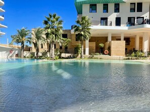 A swimming pool with clear water, surrounded by palm trees and a building with balconies. - ALLON BAY DUPLEX (R131) (Villajoyosa)