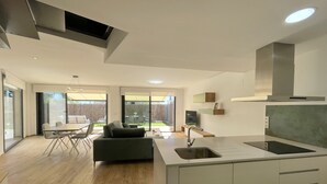 Une cuisine moderne dotée d’un îlot central, d’un coin repas avec une table et des chaises, et offrant une vue sur l’extérieur grâce à de grandes portes coulissantes.