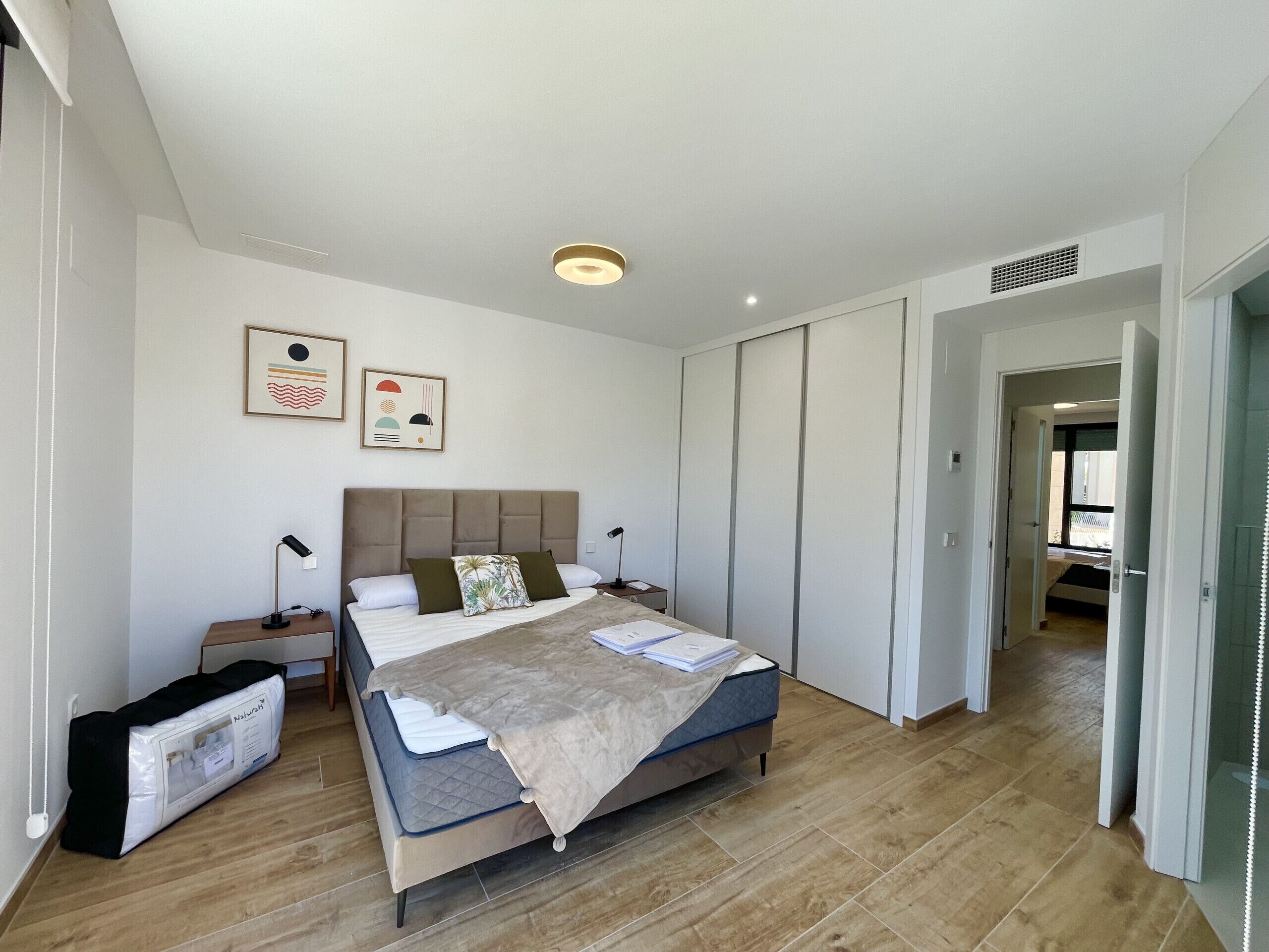 A modern bedroom with a large bed, a nightstand, a bedside table, and a wardrobe.