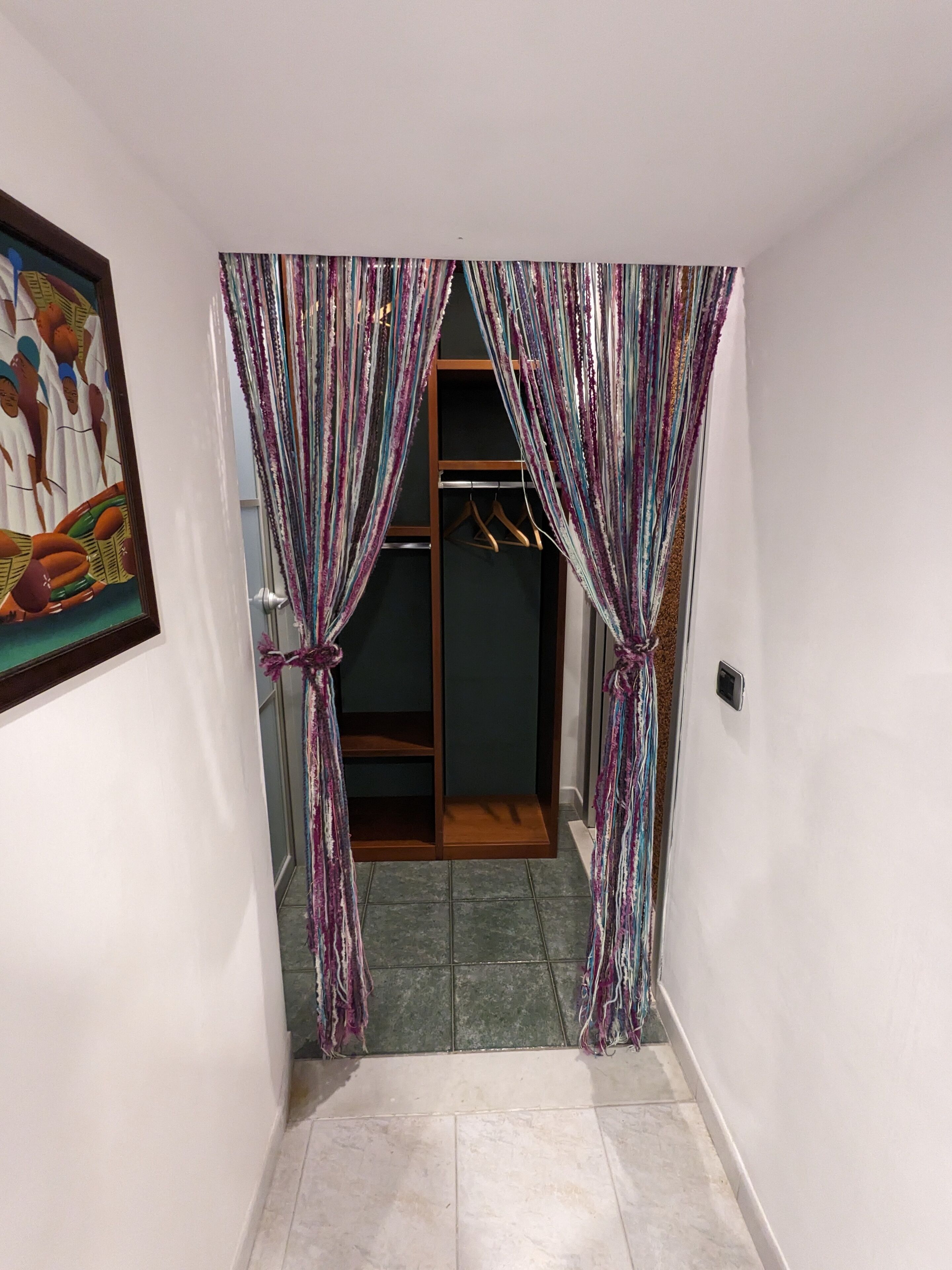 A hallway with a door leading to a room with a wooden wardrobe and a hanging rack.