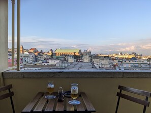 A table with two glasses of beer and a decorative item, overlooking a cityscape with historic buildings and a church. - Napoli City Panorama (Naples)