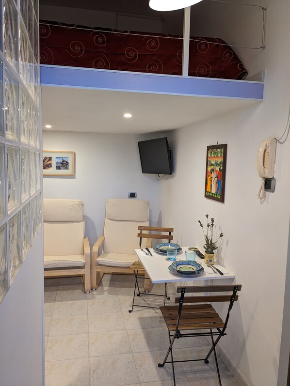 A dining area with a table set for two, two chairs, a TV mounted on the wall, and a telephone. - Napoli City Panorama (Naples)