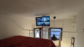 A hotel room with a bed, a TV mounted on the wall, a window with a view, and a kitchen area with a kettle. - Napoli City Panorama (Naples)