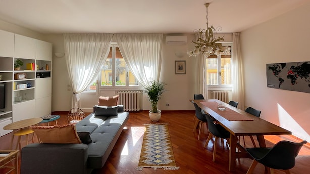 Ett modernt vardagsrum med en soffa, ett matbord och stolar. Det finns ett stort fönster med gardiner, en krukväxt och en världskarta på väggen.