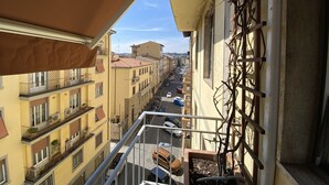En balkong med utsikt över en stadsgata, med flera byggnader och parkerade bilar.
