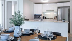 Une cuisine moderne avec des meubles blancs, un réfrigérateur en acier inoxydable et un îlot central doté d’un four à micro-ondes et d’une machine à café.
