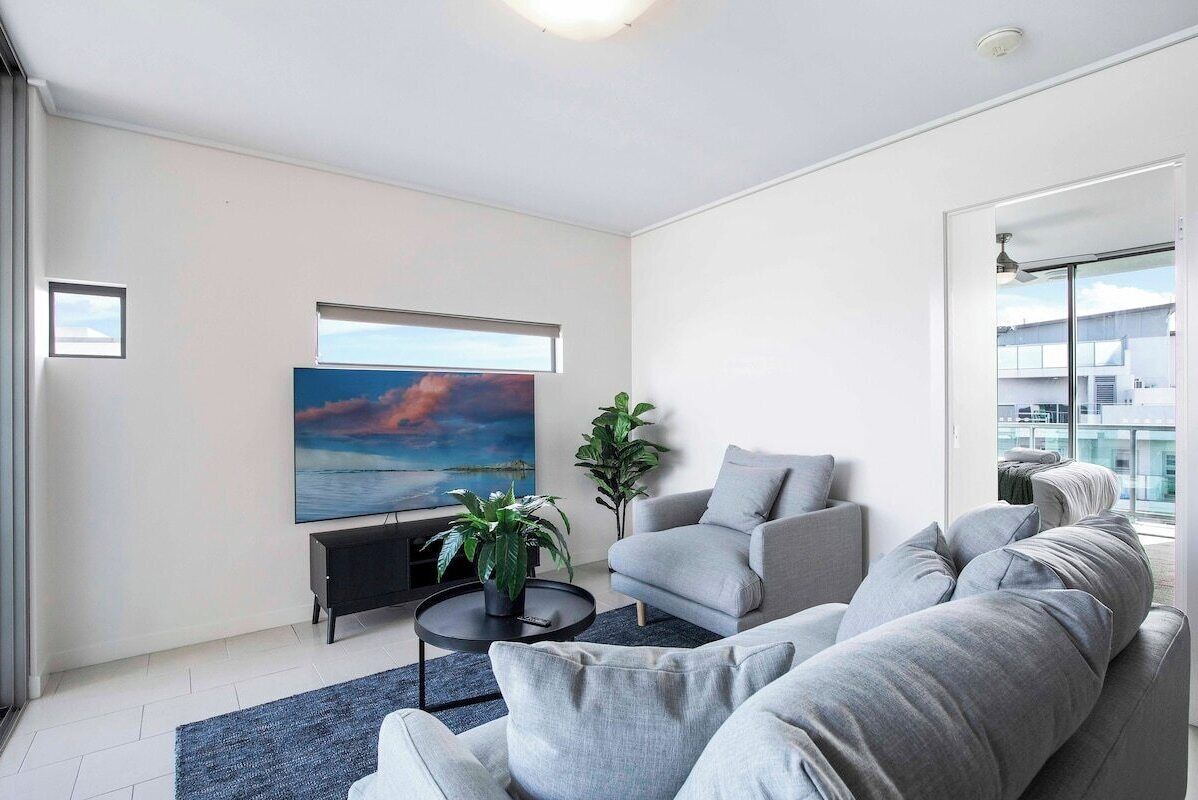 En moderne stue med en grå sofa, et sort sofabord og et stort maleri af en solnedgang.