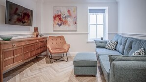 En moderne stue med fiskebensparket, et træskab, en polstret lænestol, en grå sofa med mønstrede puder og abstrakt kunst på væggene.