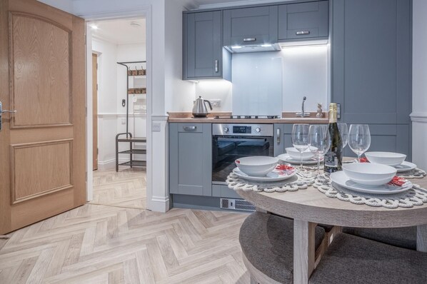 A modern kitchen with grey cabinets, a built-in oven, and a dining area set for six with white plates and glasses.