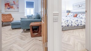 Et moderne soveværelse med fiskebensparket, seng med mønstret sengetøj, blå sofa, trænatbord og en stol.