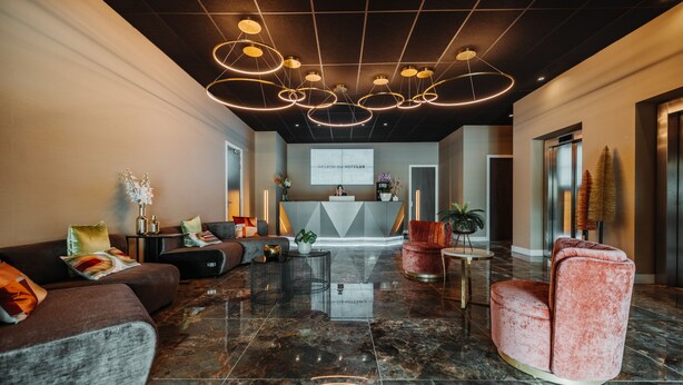 Un hall d’hôtel moderne doté d’un comptoir d’accueil, de fauteuils confortables et d’un plafond au design géométrique.