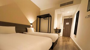 Une chambre d’hôtel avec deux lits, une table de chevet, une armoire et un miroir.