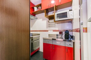 Una cocina compacta con gabinetes rojos, un microondas, un horno y una cafetera.
