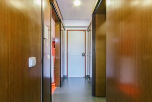 A hallway with wooden doors, a light switch, and a tiled floor.