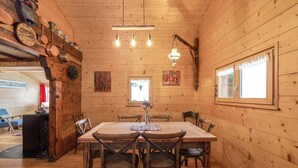 A wooden cabin interior with a dining table, chairs, and a kitchen area with pots and pans. - Chalet Gentil | Family friendly | Mountain getaway (Riddes)