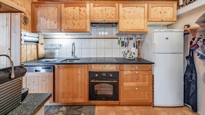 A compact kitchen with wooden cabinets, a built-in oven, a sink, and a refrigerator. - Chalet Gentil | Family friendly | Mountain getaway (Riddes)
