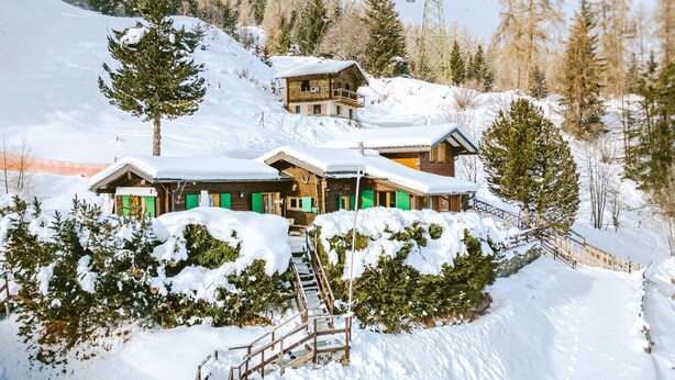 A snow-covered lodge with multiple wooden buildings, a staircase leading to the entrance, and a forested backdrop. - Chalet Gentil | Family friendly | Mountain getaway (Riddes)