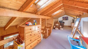 A wooden attic room with a sloped ceiling, a wooden dresser, a teddy bear, a chair, and a toy car. - Chalet Theo |Family retreat | Contemporary design (Riddes)