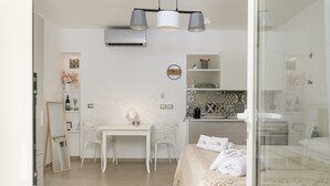 A modern, well-lit room with a dining table, chairs, a bed with a white bedspread, and a large mirror. - Almond Tree Suite (Ostuni)
