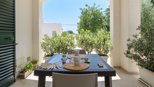 An outdoor dining area with a table set for two, surrounded by potted plants and a clear view of the sky. - Almond Tree Suite (Ostuni)