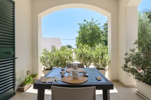 An outdoor dining area with a table set for two, surrounded by potted plants and a clear view of the sky.