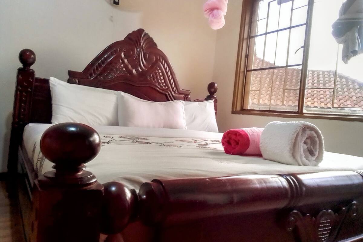 A wooden bed with a headboard, white bedding, and a rolled towel.