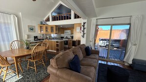Een ruime woonkamer met een hoge plafond, een eettafel met stoelen, een bank en een keuken met houten kastjes.