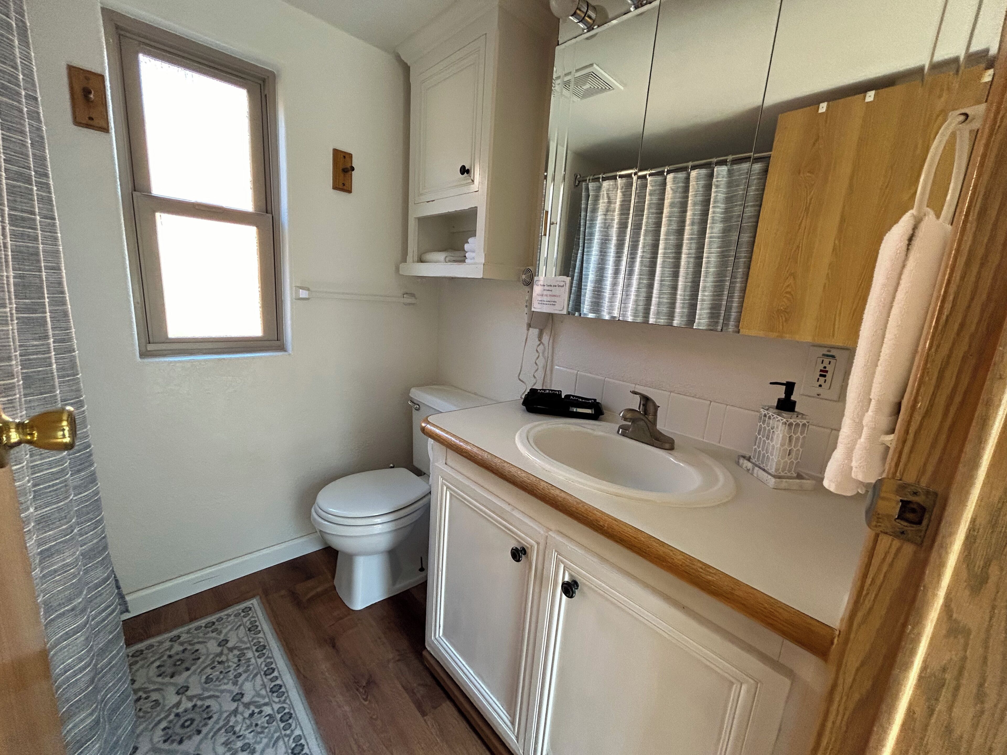 A bathroom with a toilet, sink, and mirror. There is a window, a towel rack, and a shower curtain.
