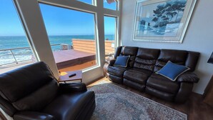 Ein Wohnzimmer mit Ledersofa, einem kleinen Tisch und einem Teppich. Ein großes Fenster bietet Blick auf den Ozean.