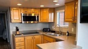 A compact kitchen with wooden cabinets, a stainless steel microwave, a toaster, and a sink. - Private Cabin 21 with Jacuzzi and Spacious Deck with View and Outdoor Seating (Private Beach Owned by White Rock Resort) (Smith River)