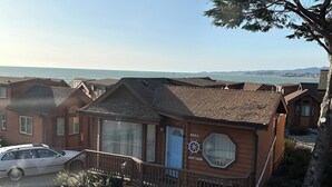A coastal cottage with a wooden exterior, a visible garage, and a clear view of the sea. - Private Cabin 21 with Jacuzzi and Spacious Deck with View and Outdoor Seating (Private Beach Owned by White Rock Resort) (Smith River)