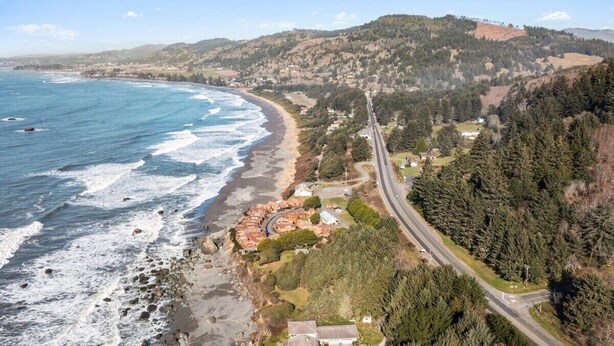 A coastal road with a beach on one side and a forested hill on the other. - Private Cabin 21 with Jacuzzi and Spacious Deck with View and Outdoor Seating (Private Beach Owned by White Rock Resort) (Smith River)