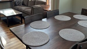 A dining area with a dark wooden table, multiple round placemats, a sofa, and a view through large windows. - Private Cabin 21 with Jacuzzi and Spacious Deck with View and Outdoor Seating (Private Beach Owned by White Rock Resort) (Smith River)