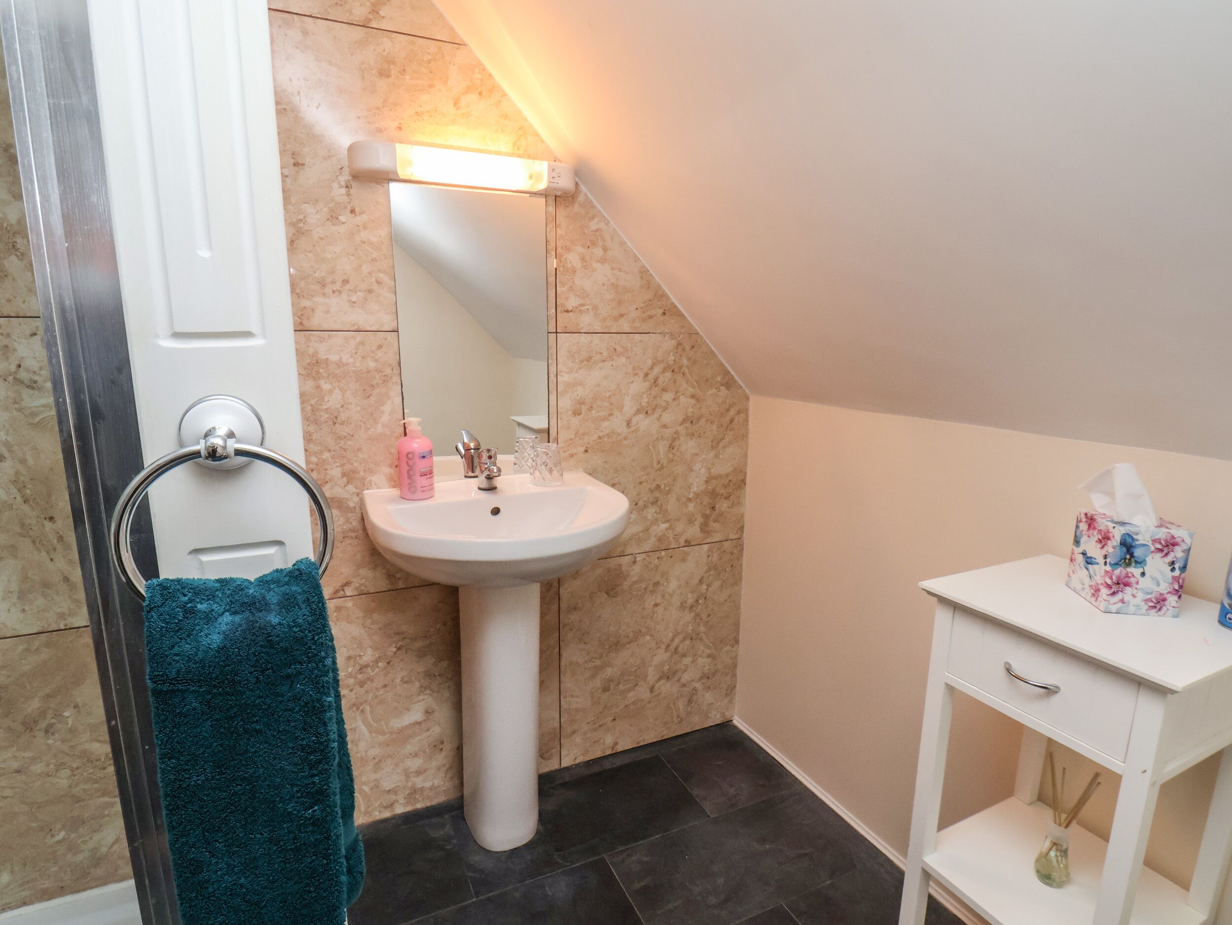 A bathroom with a white sink, a mirror, a towel rack, a small white cabinet, and a shower area.