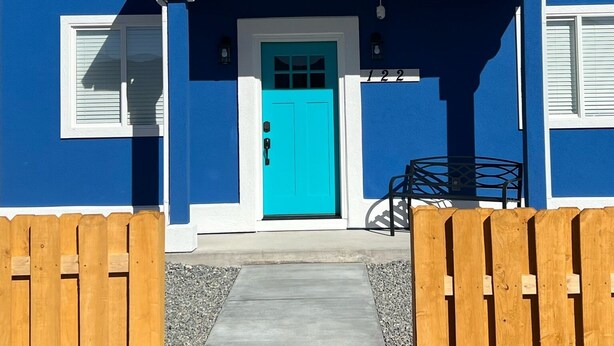Una casa azul con una puerta turquesa, contraventanas blancas y cerca de madera.