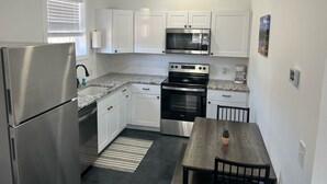 Una cocina compacta con armarios blancos, un refrigerador de acero inoxidable, un microondas, un horno y una cafetera.