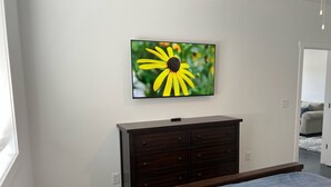 Un dormitorio con una cama, un tocador y un televisor de pared que muestra una flor.