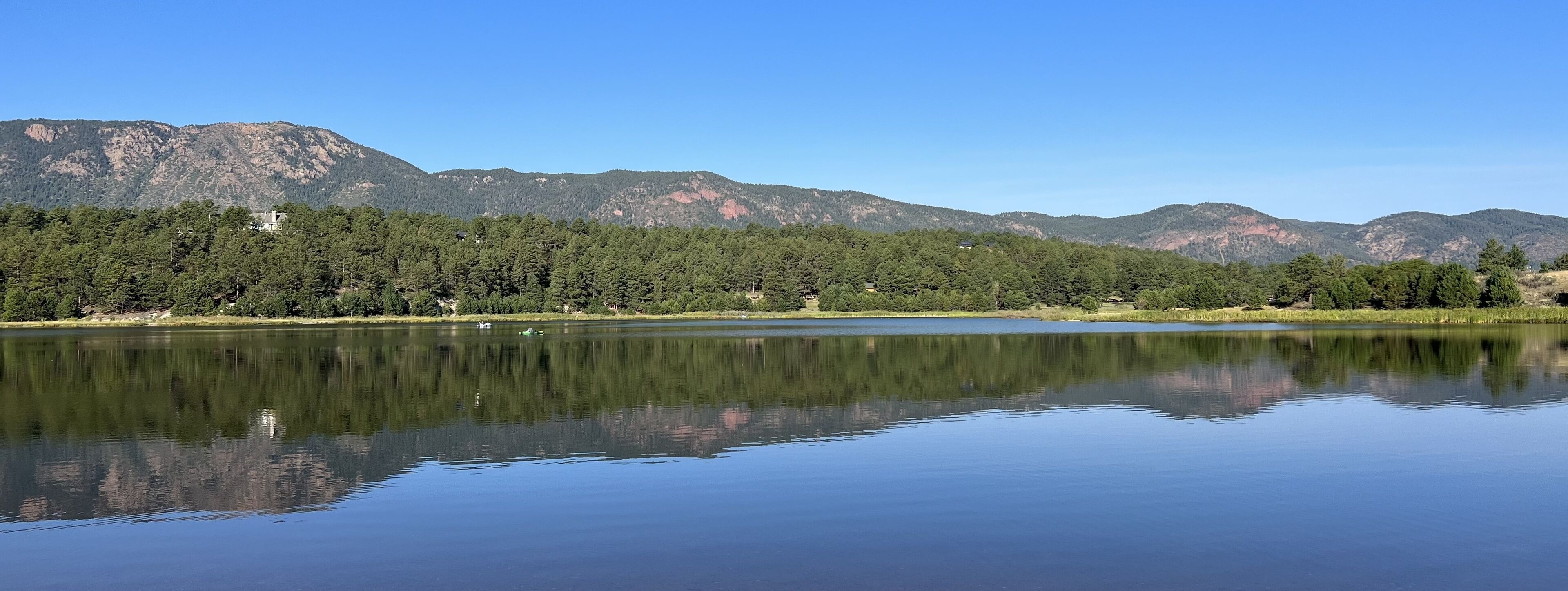 A calm lake with a reflection of the surrounding mountains and trees.